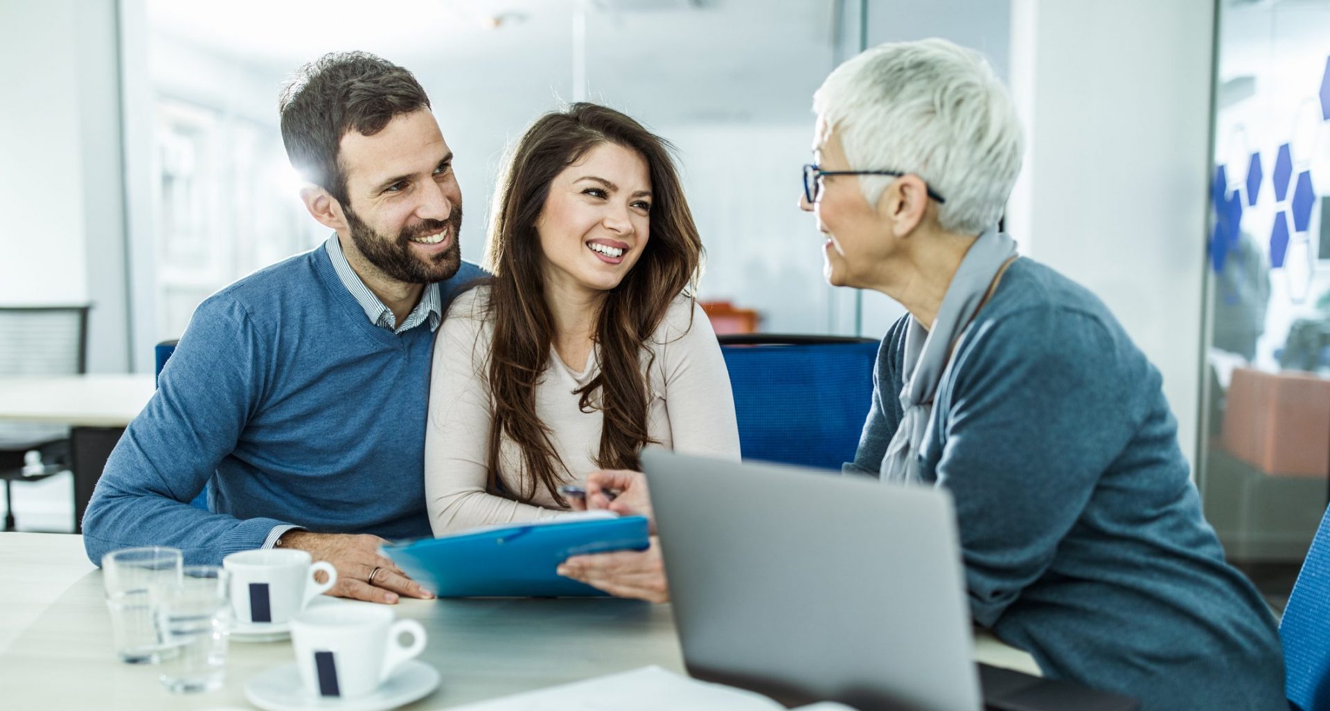 Young happy couple communicating with their mature financial advisor on a meeting in the office.