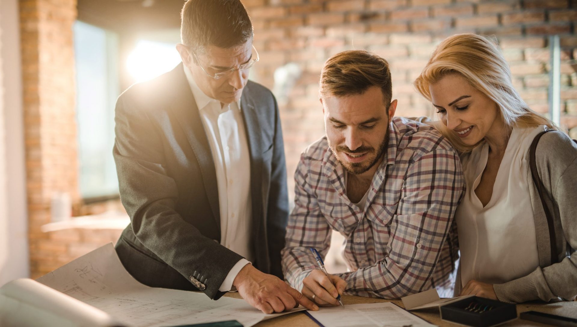 Mid adult investor showing young couple where to sign the contract for buying a house.