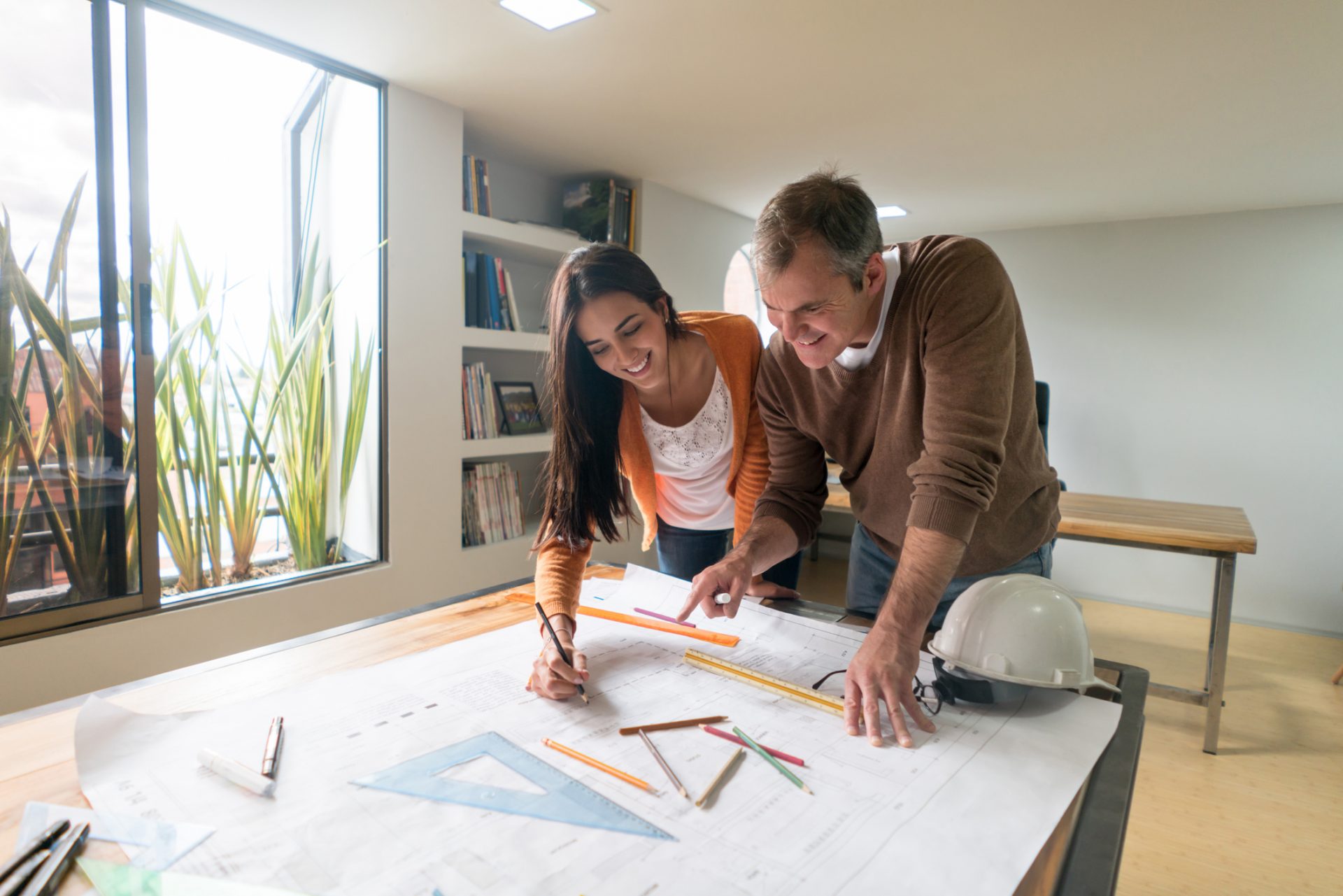 Portrait of a couple of architects working at the office drawing a blueprint and looking very happy