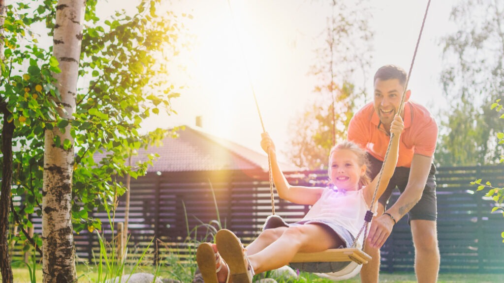 Joyous Father Pushes Swings with His Cute Little Daughter on Them. Happy Family Spends Time Together one Sunny Summer Day in the Idyllics Backyard.