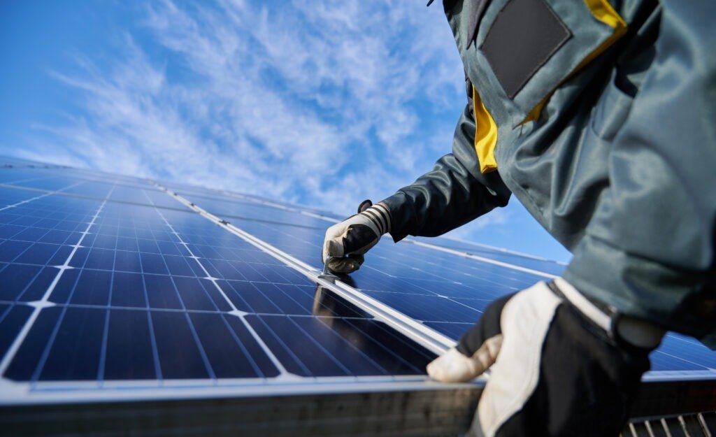 Close up of man technician in work gloves installing stand-alone photovoltaic solar panel system under beautiful blue sky with clouds. Concept of alternative energy and power sustainable resources.